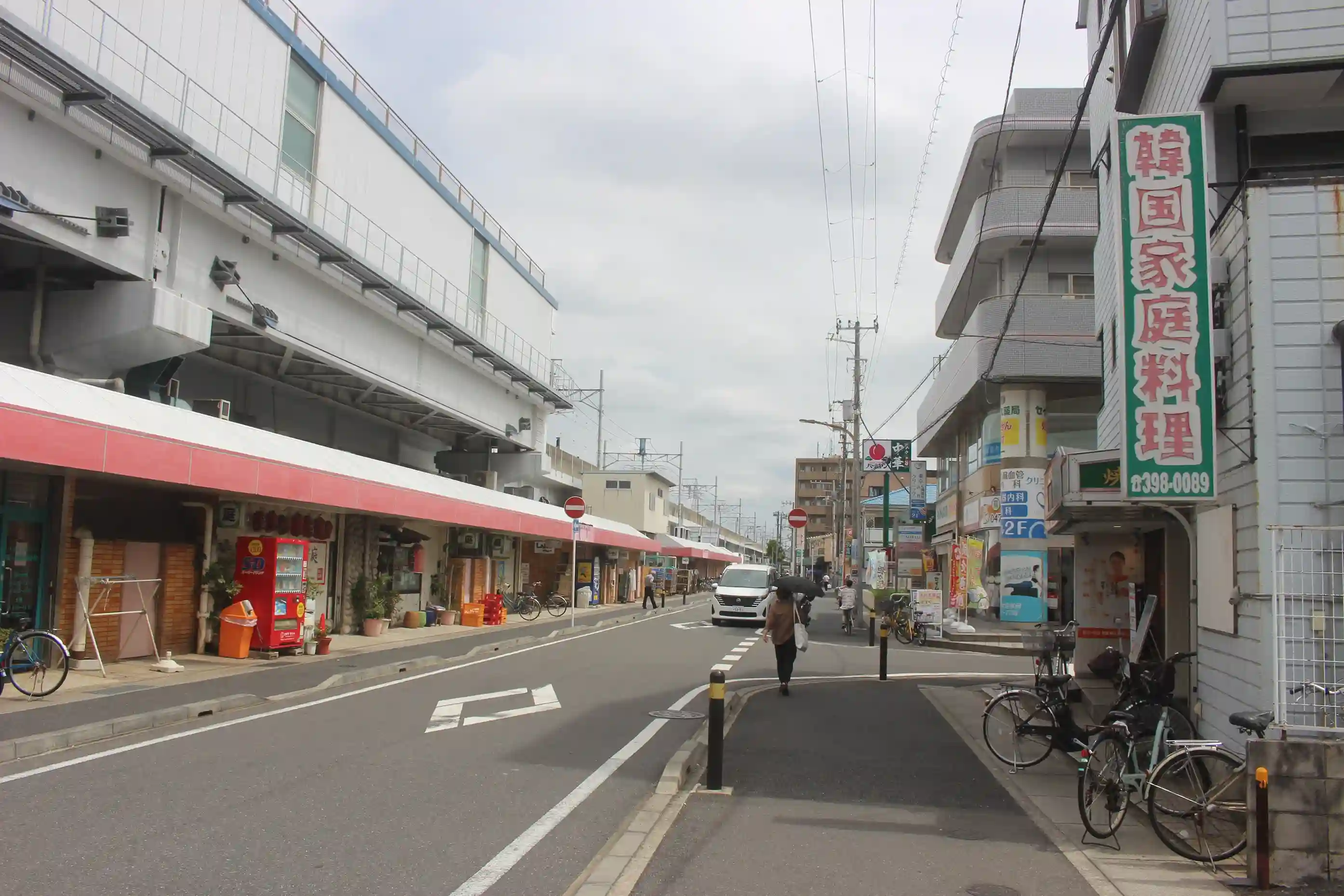 左手に東西線の高架、右手に焼肉店「明洞（みょんどん）」がある直線道路。この道を道なりにまっすぐ進みます。