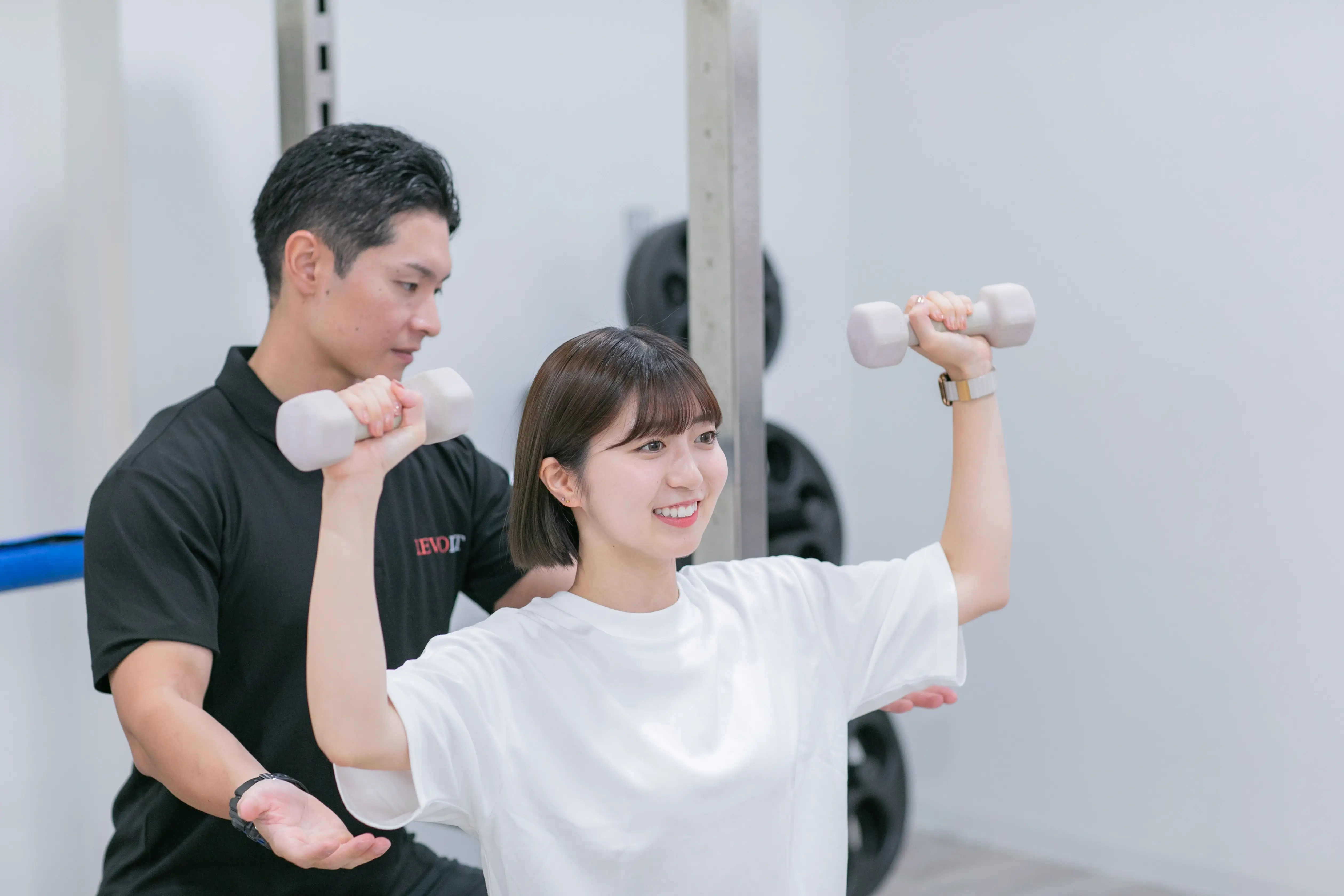 浦安のパーソナルジムREVOISTで、トレーナーのサポートを受けながら笑顔でトレーニングをする運動初心者の女性