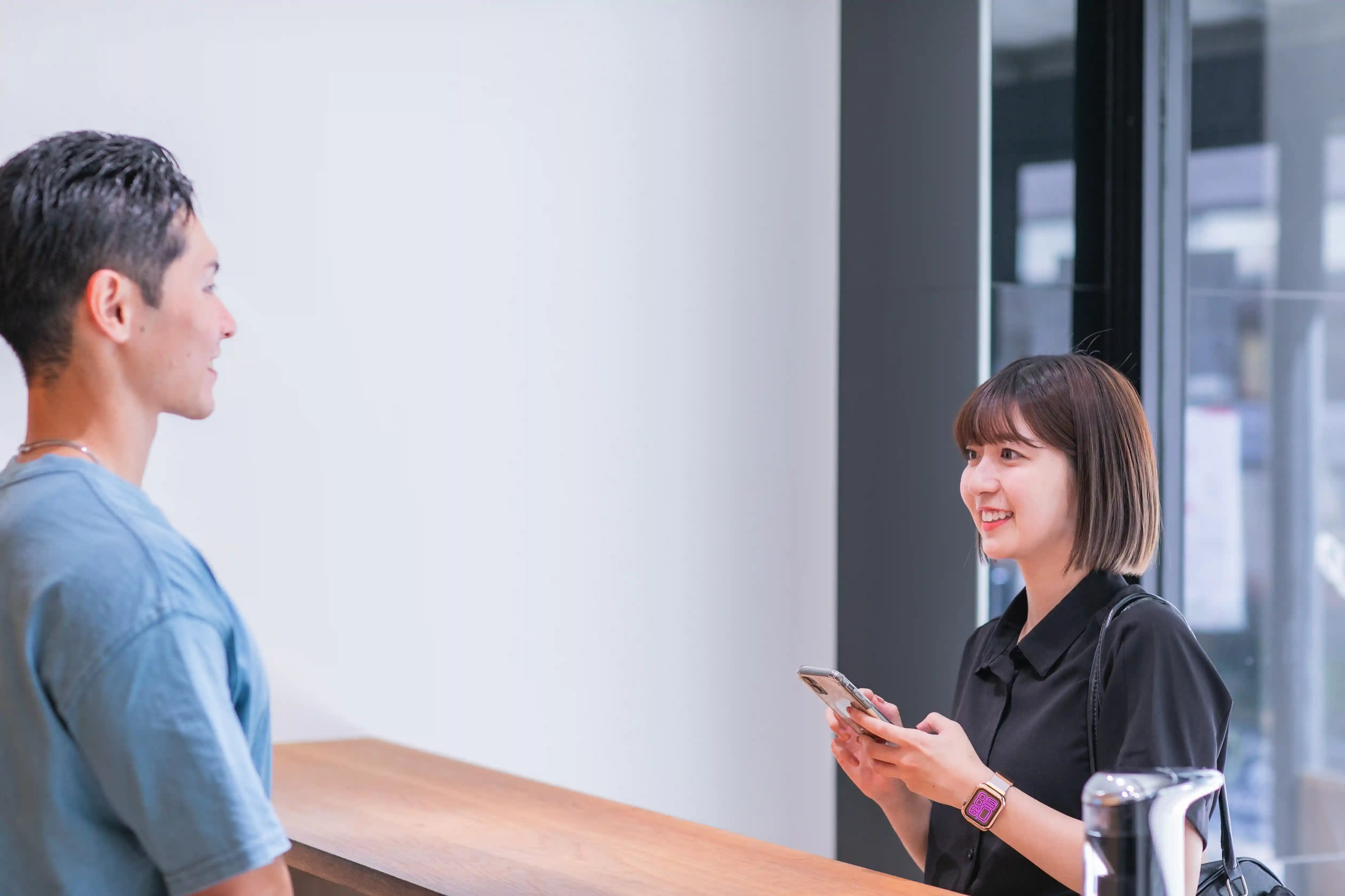 浦安のパーソナルジム「REVOIST」にスマホから予約して来店し、笑顔で受付をする女性。駅近で複数店舗に通いやすい環境です。